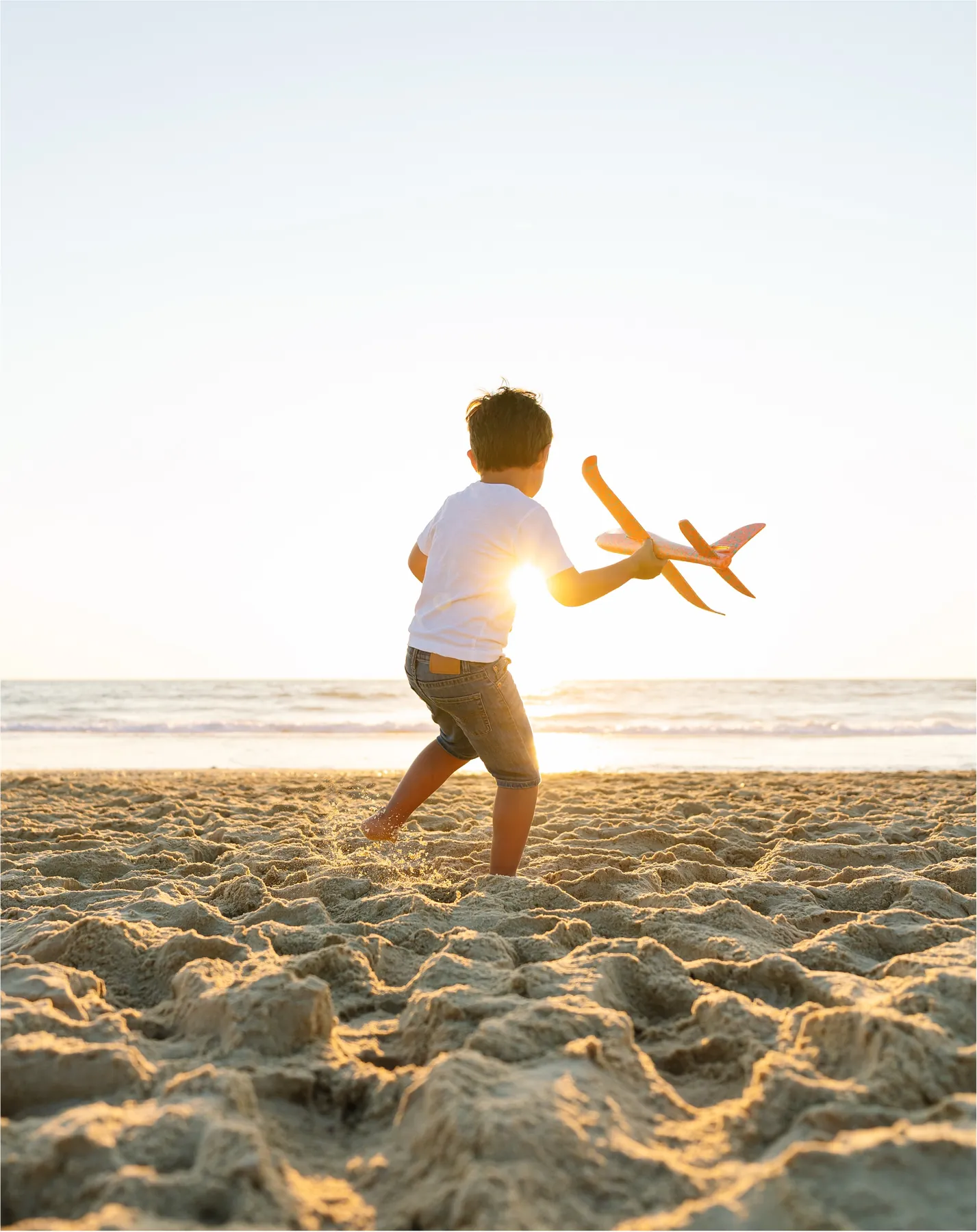 A child flying a toy plane on the beach at sunrise