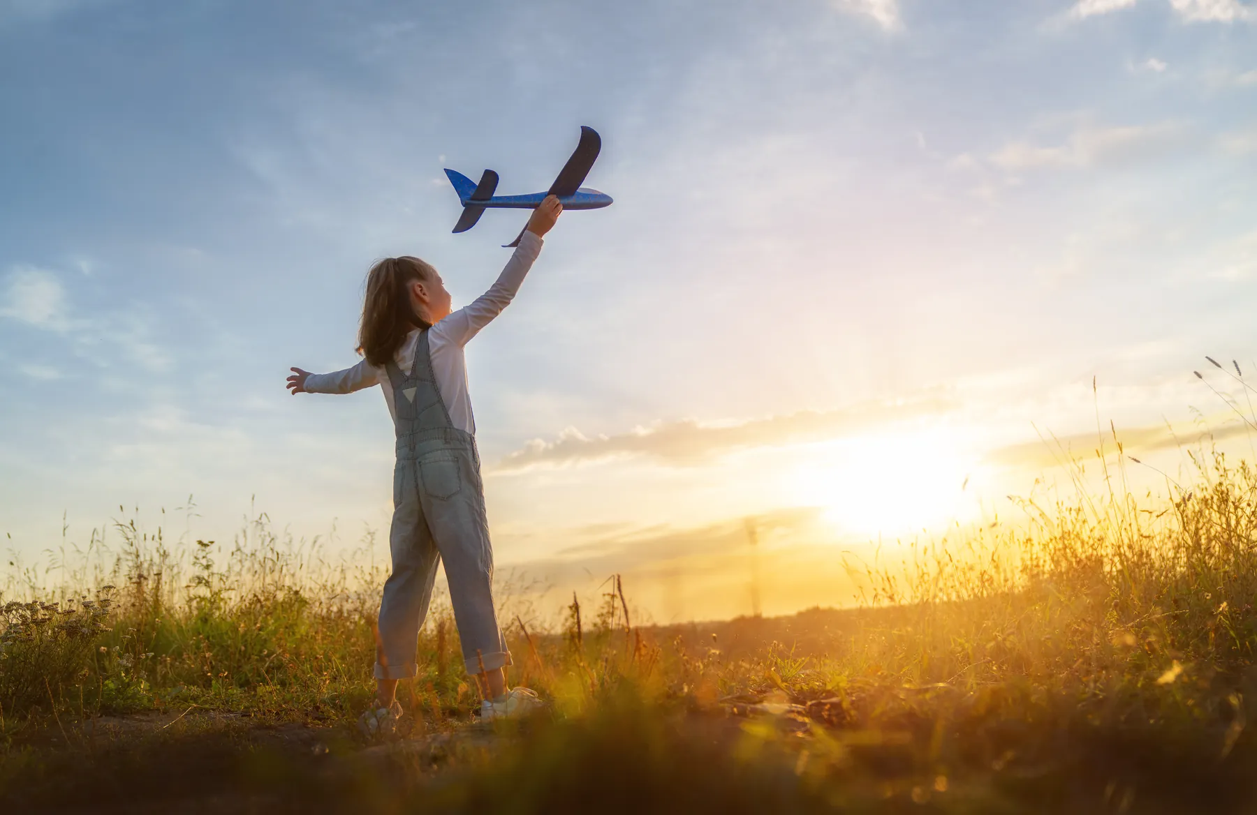A child holding a toy plane towards the sunrise